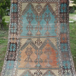 Puede incluir: Una alfombra turca vintage con un patr&oacute;n geom&eacute;trico tradicional en tonos azules, marrones y beige. La alfombra presenta un dise&ntilde;o central de &aacute;rboles estilizados y motivos florales.