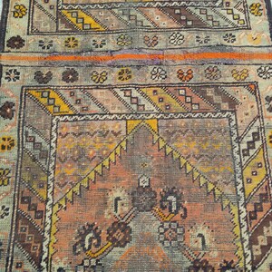 May include: A vintage rug with a geometric pattern in shades of brown, orange, yellow, and white. The rug has a faded, worn look, giving it a rustic and antique feel.