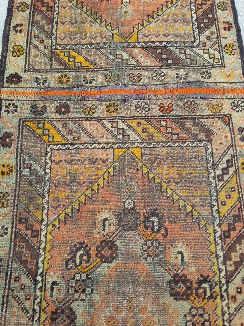 May include: A vintage rug with a geometric pattern in shades of brown, orange, yellow, and white. The rug has a faded, worn look, giving it a rustic and antique feel.