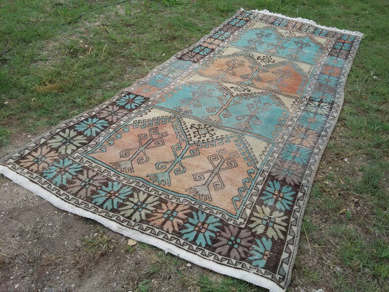 Puede incluir: Una alfombra rectangular larga con un dise&ntilde;o turco tradicional. La alfombra presenta un patr&oacute;n repetitivo de formas geom&eacute;tricas en tonos de azul, marr&oacute;n y beige.