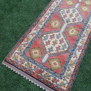 May include: A long, narrow rug with a geometric pattern in shades of red, blue, green, and white. The rug has a crocheted border.