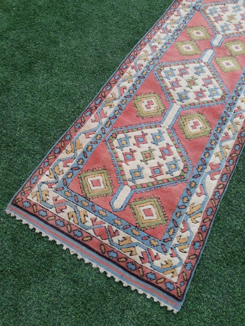 May include: A long, narrow rug with a geometric pattern in shades of red, blue, green, and white. The rug has a crocheted border.