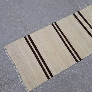 May include: A white and brown striped rug with a fringed edge. The rug is made of natural fibres and has a rustic look.