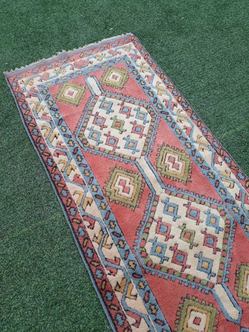 May include: A red, blue, and green patterned rug with a geometric design. The rug has a fringed edge and is laid out on a green surface.