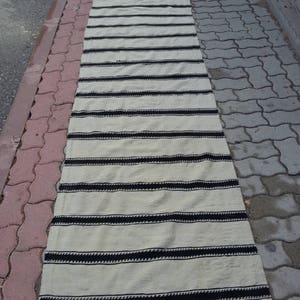Pu&ograve; includere: Un tappeto a strisce bianche e nere con un design intrecciato. Il tappeto &egrave; steso su un vialetto di mattoni grigi.