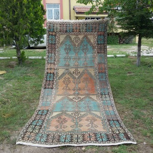 Puede incluir: Una alfombra turca vintage con un patr&oacute;n geom&eacute;trico en tonos azules, naranjas y marrones. La alfombra tiene un borde con flecos y est&aacute; colocada sobre una superficie de c&eacute;sped.