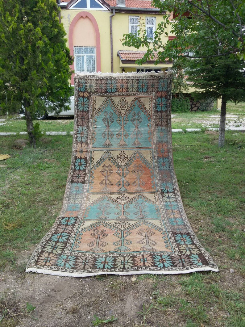 Puede incluir: Una alfombra turca vintage con un patr&oacute;n geom&eacute;trico en tonos azules, naranjas y marrones. La alfombra tiene un borde con flecos y est&aacute; colocada sobre una superficie de c&eacute;sped.