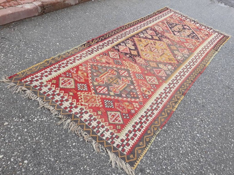 May include: A vintage Turkish rug with a geometric pattern in shades of red, brown, beige, and white. The rug has a fringe border and is woven with intricate details.