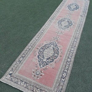 May include: A long, pink runner rug with a floral pattern and a border of intricate designs. The rug has a faded, vintage look and is made of wool.