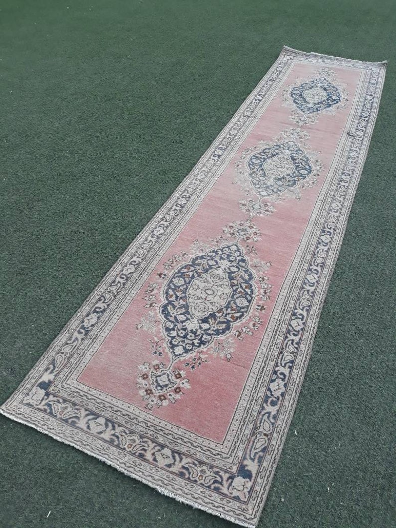 May include: A long, pink runner rug with a floral pattern and a border of intricate designs. The rug has a faded, vintage look and is made of wool.