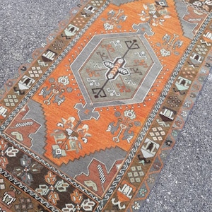 May include: A vintage Turkish rug with a geometric pattern in shades of orange, brown, and gray. The rug has a central medallion and a border with a repeating design.