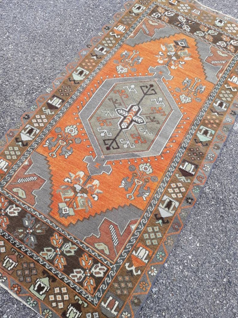 May include: A vintage Turkish rug with a geometric pattern in shades of orange, brown, and gray. The rug has a central medallion and a border with a repeating design.