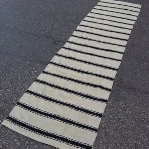 Pu&ograve; includere: Un lungo tappeto da corridoio bianco con strisce nere. Il tappeto &egrave; realizzato in tessuto tessuto e ha un design semplice e moderno.