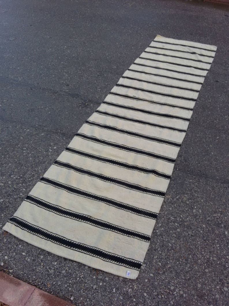Pu&ograve; includere: Un lungo tappeto da corridoio bianco con strisce nere. Il tappeto &egrave; realizzato in tessuto tessuto e ha un design semplice e moderno.