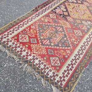 May include: A traditional Turkish rug with a geometric pattern in shades of red, white, black, and beige. The rug has a fringe border.