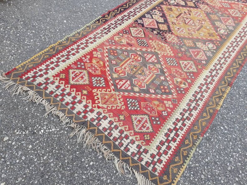 May include: A traditional Turkish rug with a geometric pattern in shades of red, white, black, and beige. The rug has a fringe border.