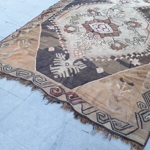 May include: A vintage Turkish rug with a brown, beige, and white geometric pattern. The rug has a fringe border and is woven with a variety of textures.