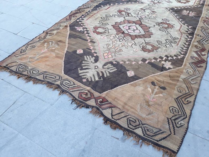 May include: A vintage Turkish rug with a brown, beige, and white geometric pattern. The rug has a fringe border and is woven with a variety of textures.