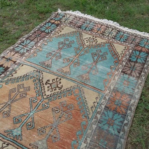 Puede incluir: Una alfombra turca vintage con un patr&oacute;n geom&eacute;trico en tonos azules, naranjas y marrones. La alfombra tiene un borde con flecos y est&aacute; tejida con un dise&ntilde;o tradicional.