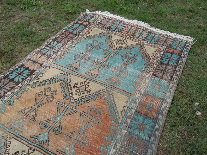Puede incluir: Una alfombra turca vintage con un patr&oacute;n geom&eacute;trico en tonos azules, naranjas y marrones. La alfombra tiene un borde con flecos y est&aacute; tejida con un dise&ntilde;o tradicional.