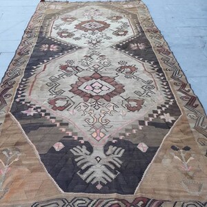 May include: A vintage Turkish rug with a geometric pattern in shades of brown, beige, and pink. The rug has a fringed edge and is woven with intricate details.