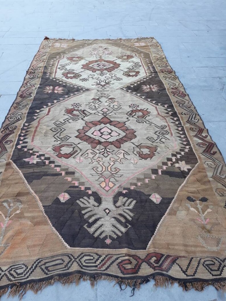 May include: A vintage Turkish rug with a geometric pattern in shades of brown, beige, and pink. The rug has a fringed edge and is woven with intricate details.