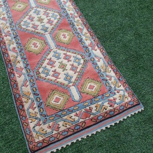 May include: A vintage runner rug with a geometric pattern in shades of red, blue, green, and cream. The rug has a fringed edge.
