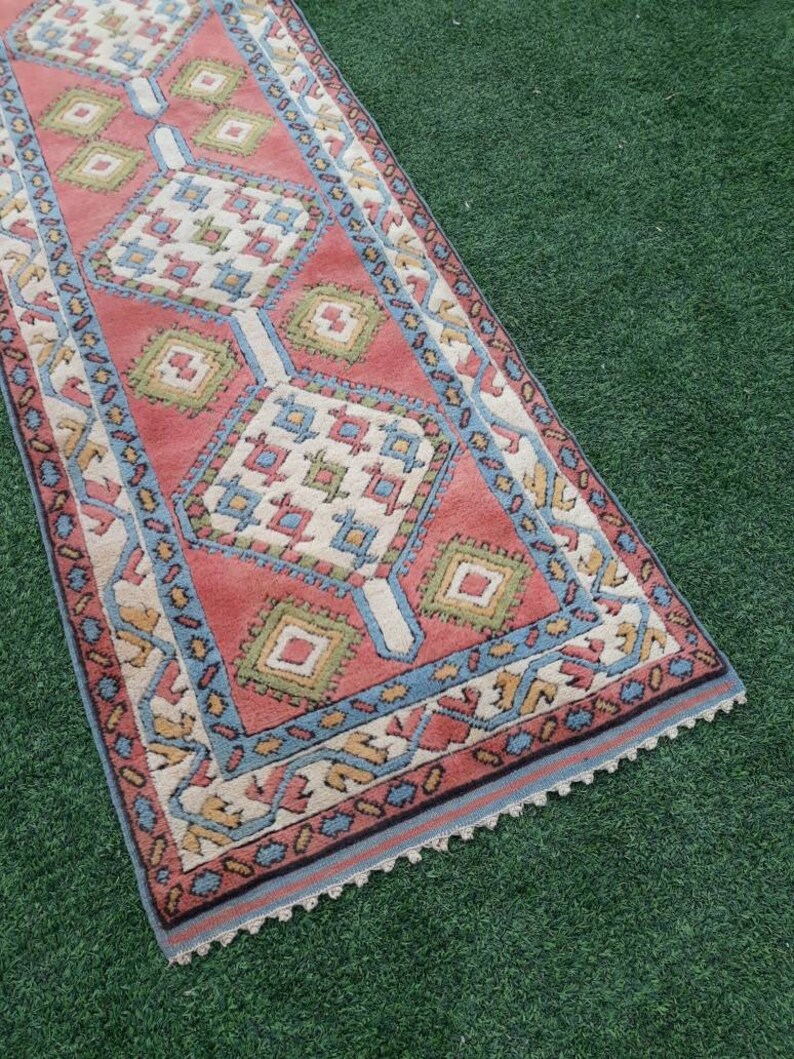 May include: A vintage runner rug with a geometric pattern in shades of red, blue, green, and cream. The rug has a fringed edge.