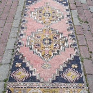 May include: A pink and navy blue runner rug with a traditional geometric pattern. The rug has a faded, vintage look and is made of wool.