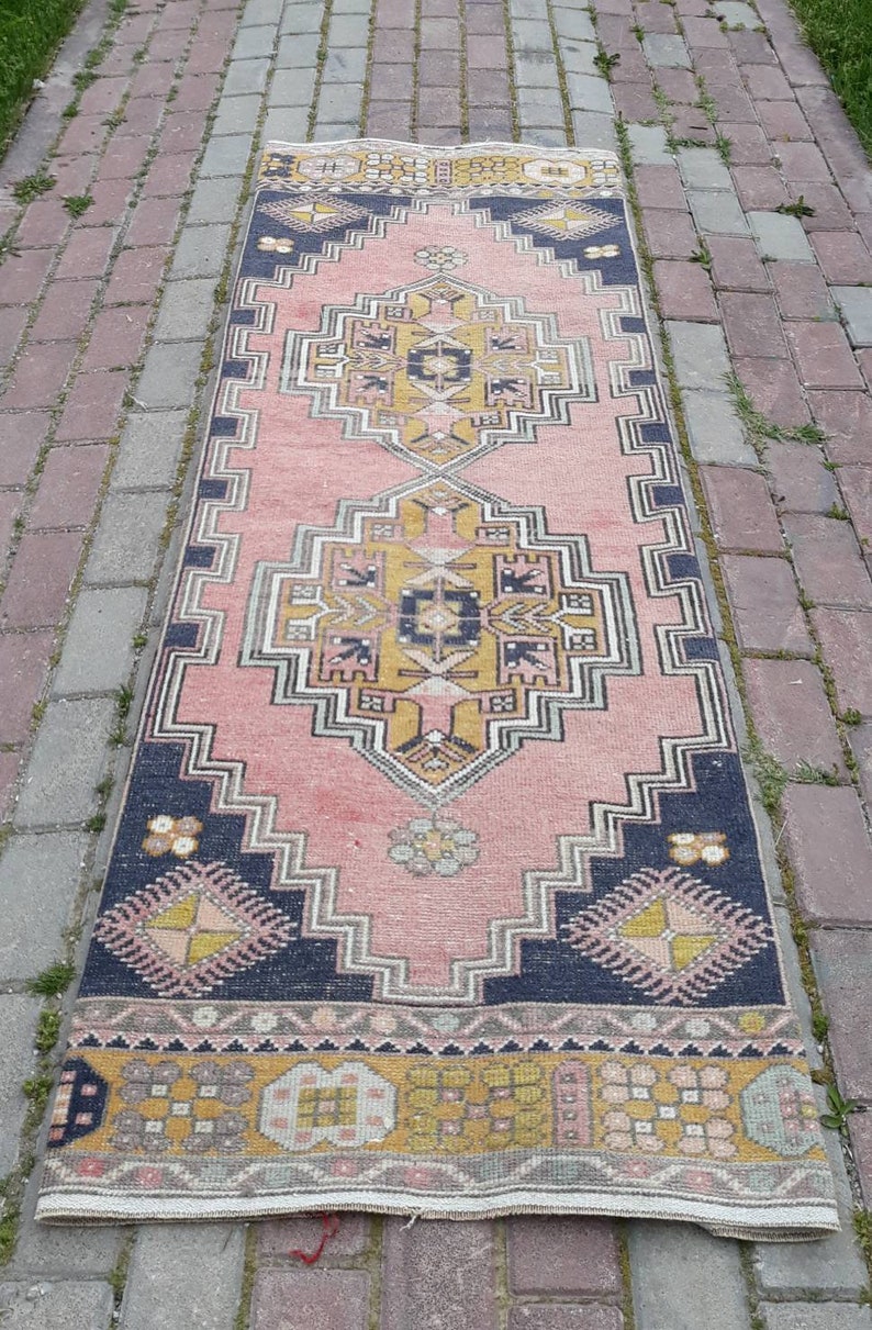 May include: A pink and navy blue runner rug with a traditional geometric pattern. The rug has a faded, vintage look and is made of wool.
