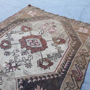 May include: A vintage Turkish rug with a geometric pattern in shades of brown, pink, and white. The rug has a worn and faded look, giving it a rustic and antique feel.