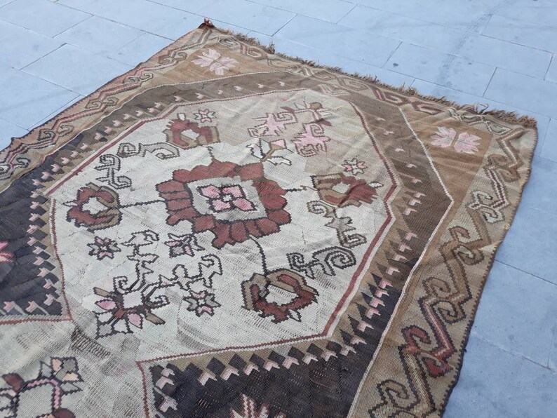 May include: A vintage Turkish rug with a geometric pattern in shades of brown, pink, and white. The rug has a worn and faded look, giving it a rustic and antique feel.