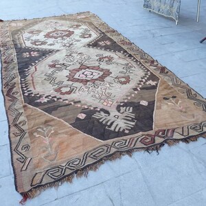 May include: A vintage Turkish rug with a brown, beige, and pink geometric pattern. The rug has a fringed edge and is made of wool.