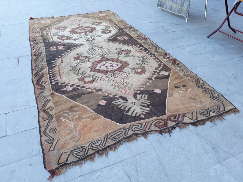May include: A vintage Turkish rug with a brown, beige, and pink geometric pattern. The rug has a fringed edge and is made of wool.