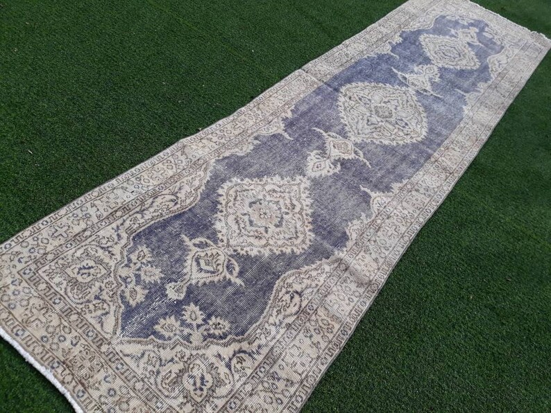 May include: A vintage runner rug with a faded blue background and intricate white and beige floral patterns. The rug has a distressed look and is perfect for adding a touch of bohemian style to any room.