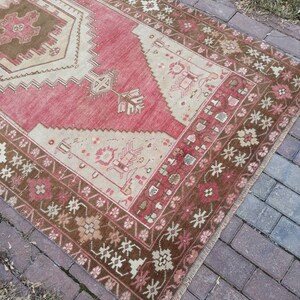 May include: A vintage Turkish runner rug with a red background and a brown and white geometric pattern. The rug has a fringe border and is made of wool.