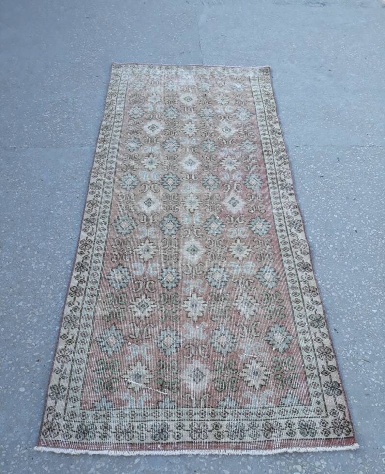 K&ouml;nnte beinhalten: Ein Vintage-L&auml;ufer mit einem rosafarbenen, wei&szlig;en und gr&uuml;nen Blumenmuster. Der Teppich hat einen abgenutzten Look und ist aus Wolle.