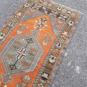 May include: A vintage Turkish rug with a geometric pattern in shades of orange, brown, and gray. The rug has a central medallion and a border with repeating motifs.