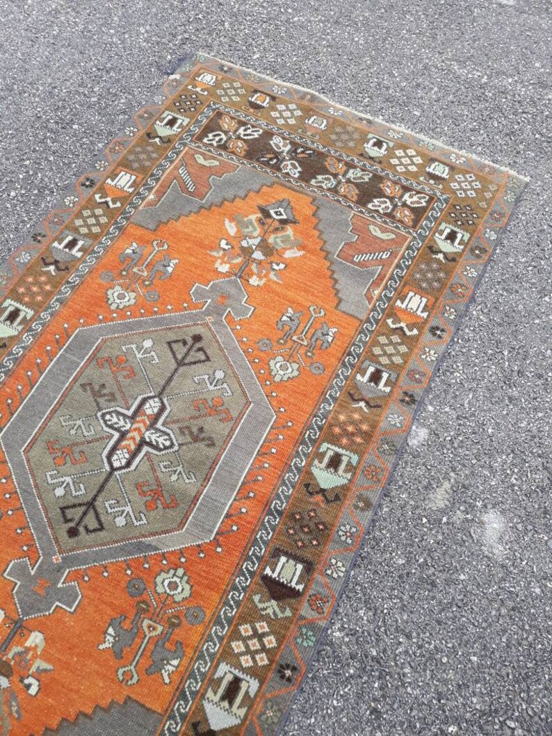 May include: A vintage Turkish rug with a geometric pattern in shades of orange, brown, and gray. The rug has a central medallion and a border with repeating motifs.