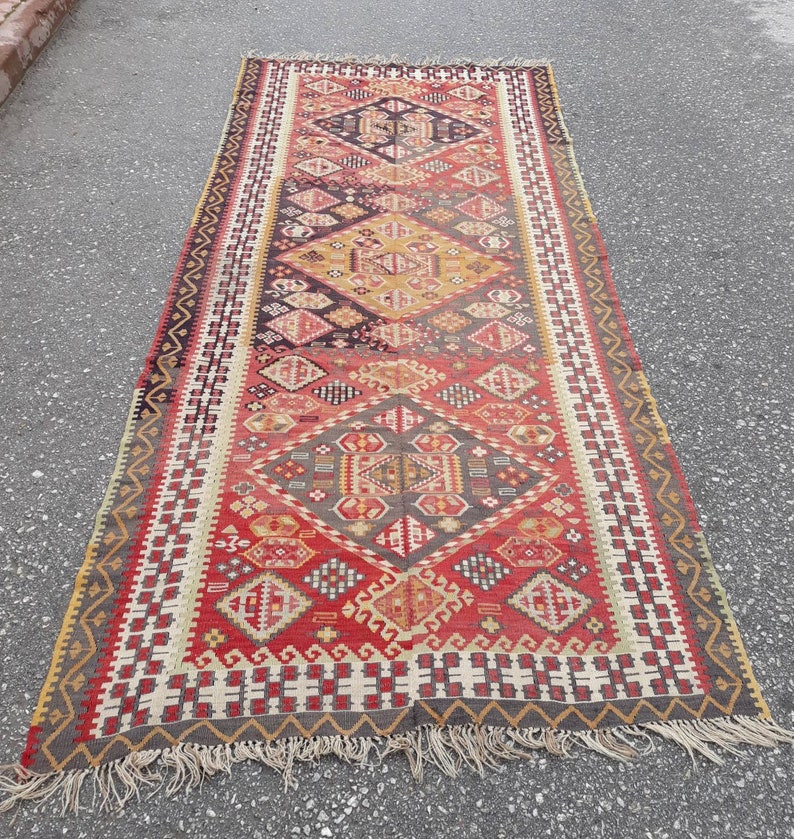 May include: A long, rectangular rug with a traditional Turkish design. The rug is woven with a variety of colors, including red, orange, yellow, blue, and green. The rug has a fringe on both ends.