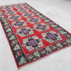 May include: A red, black, and white patterned rug with a geometric design. The rug has a fringe border and is made of wool.