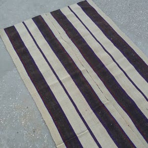 May include: A long, striped rug with alternating white and dark brown stripes. The stripes have a subtle purple and red accent.
