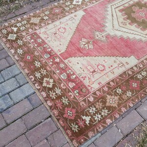 May include: A vintage Turkish rug with a red, cream, and brown color scheme. The rug has a geometric pattern with a central medallion and a border of floral motifs.