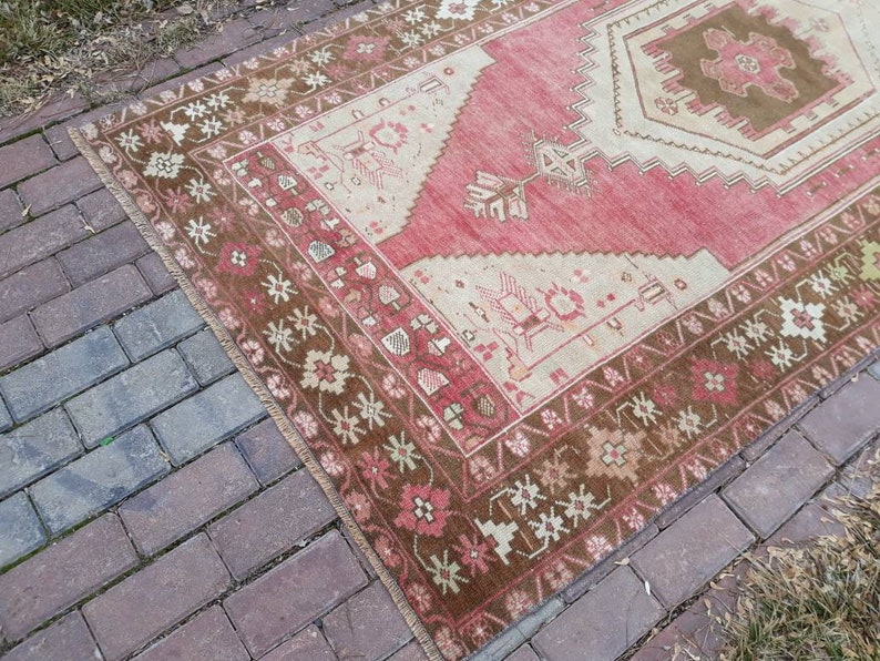 May include: A vintage Turkish rug with a red, cream, and brown color scheme. The rug has a geometric pattern with a central medallion and a border of floral motifs.
