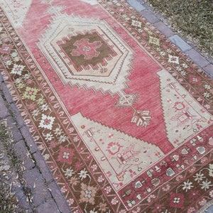 May include: A vintage Turkish rug with a pink and brown color scheme. The rug has a geometric pattern with a central medallion. The rug is in good condition and has a worn look.