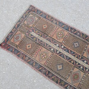 May include: A vintage runner rug with a geometric pattern in shades of brown, pink, and blue. The rug has a fringed edge and is made of wool.