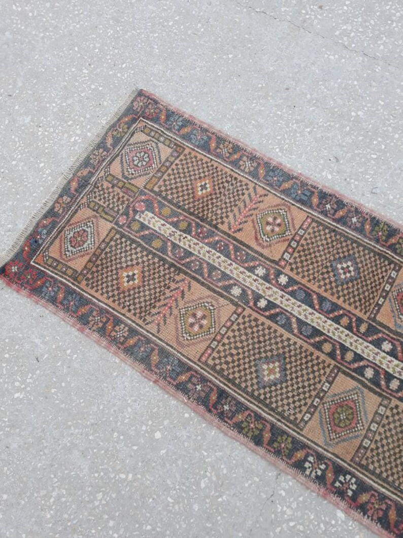 May include: A vintage runner rug with a geometric pattern in shades of brown, pink, and blue. The rug has a fringed edge and is made of wool.