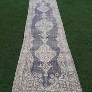 May include: A long, narrow rug with a faded, vintage look. The rug has a blue background with a white floral pattern. The rug has a fringe border.