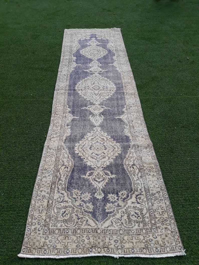 May include: A long, narrow rug with a faded, vintage look. The rug has a blue background with a white floral pattern. The rug has a fringe border.