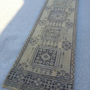 May include: A long, rectangular rug with a beige background and a black and white geometric pattern. The rug has a fringe border.